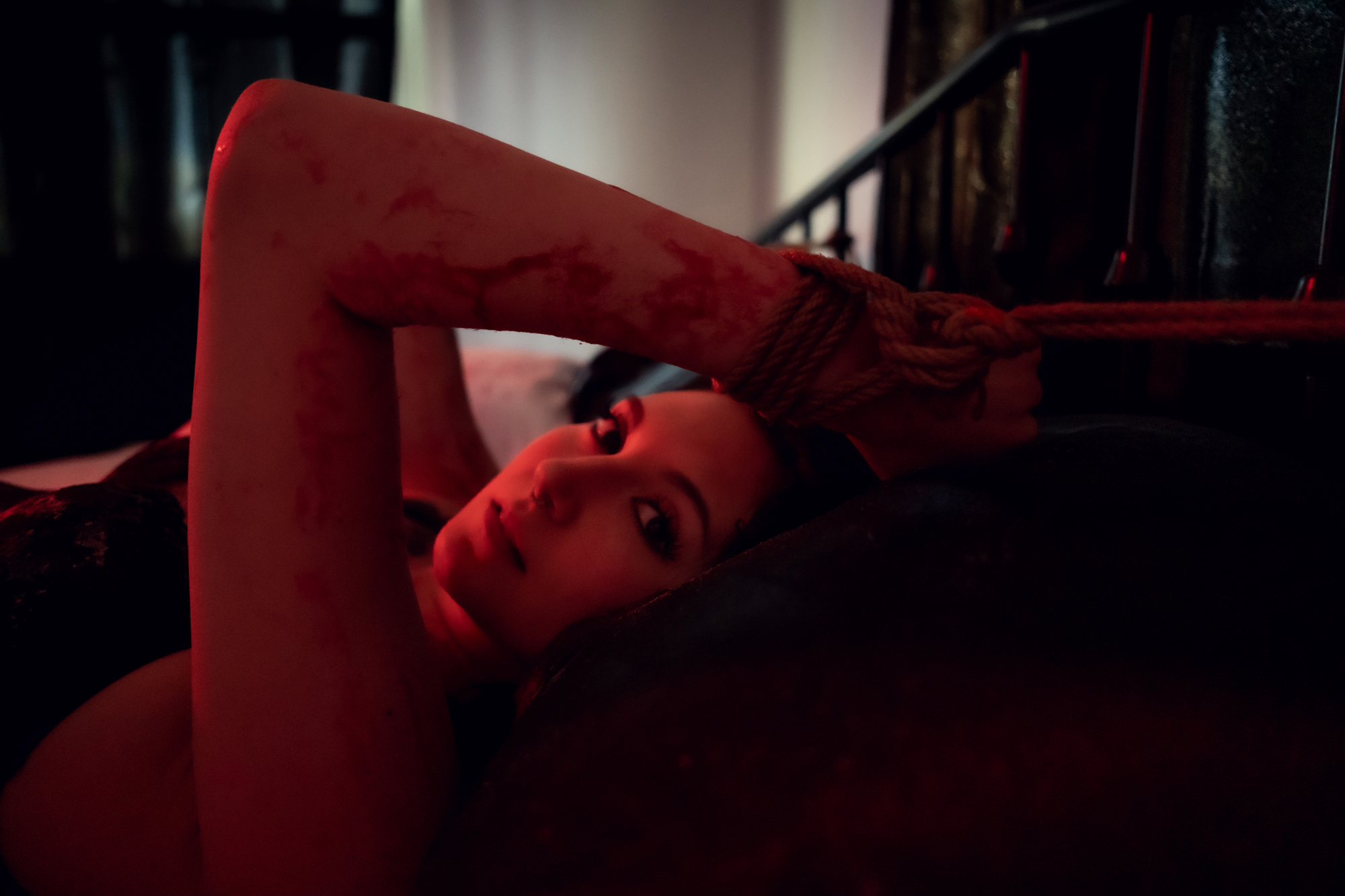 Sensual boudoir scene with a woman on a bed, featuring amazing artistic elements like faux blood and tasteful restraints.