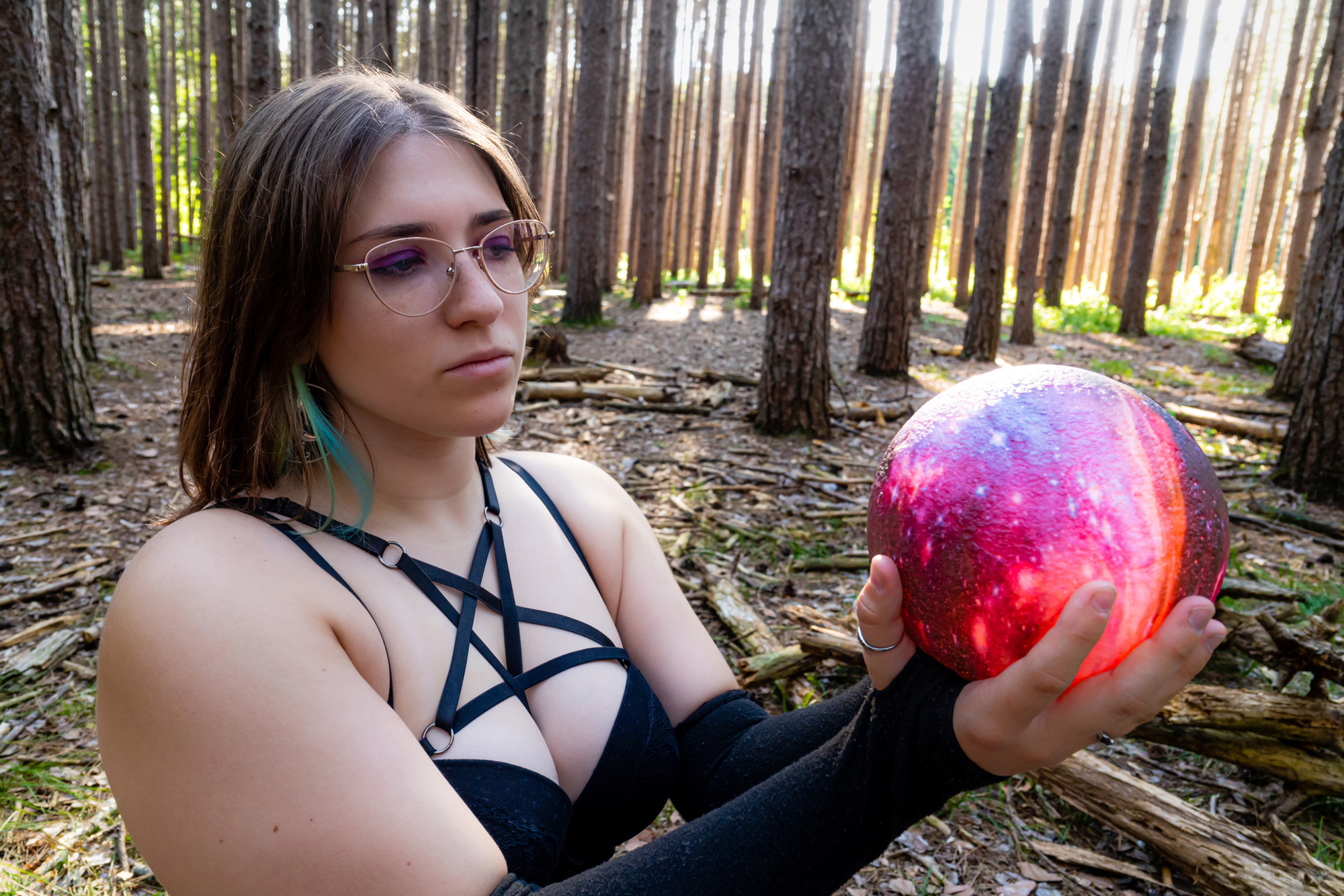 Enchanting witch in the woods, seated and gazing into a glowing galaxy orb.