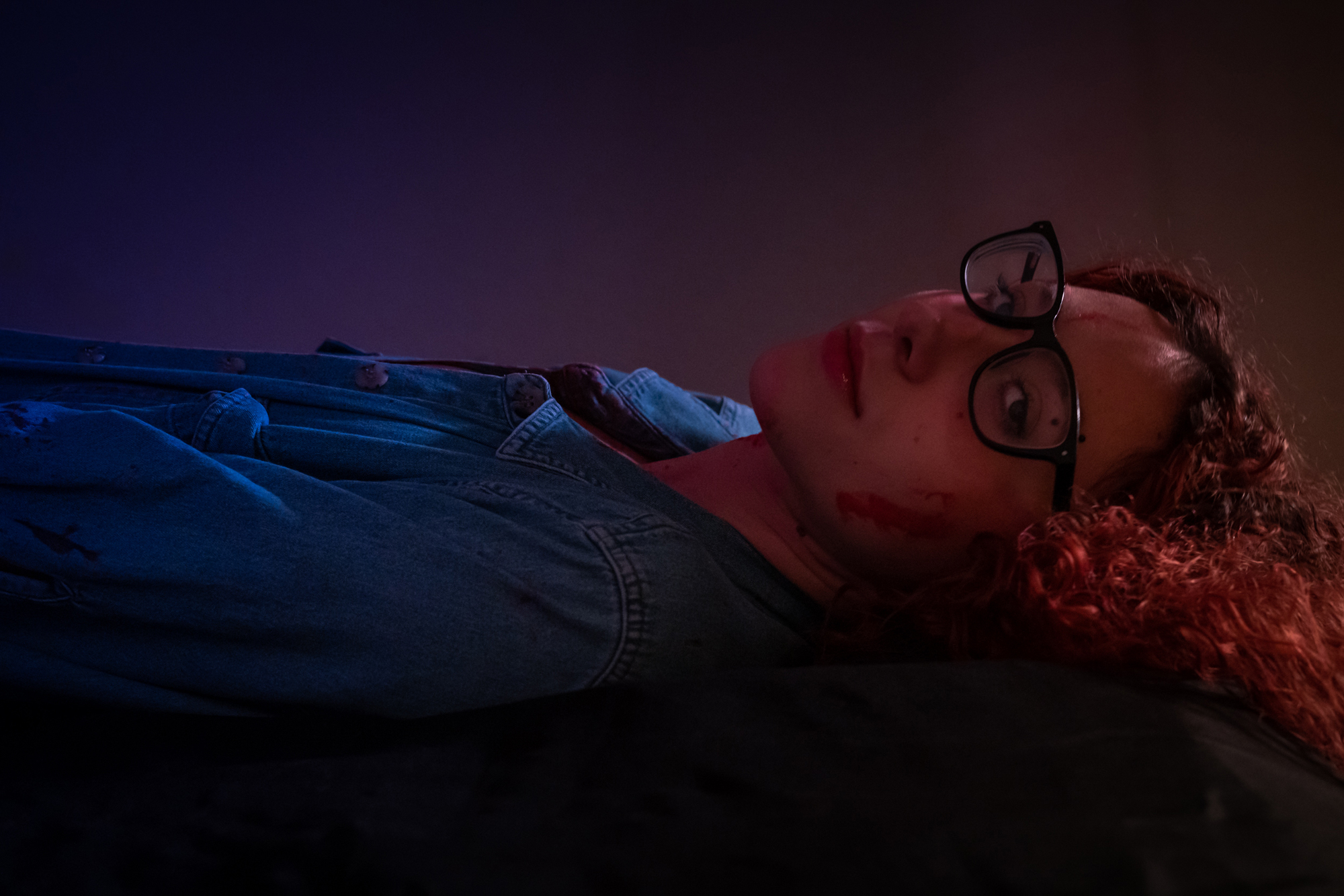 Best boudoir edge: Pretty girl in a jean jacket, laying on a bed with faux blood on her face, creating a captivating and daring scene.