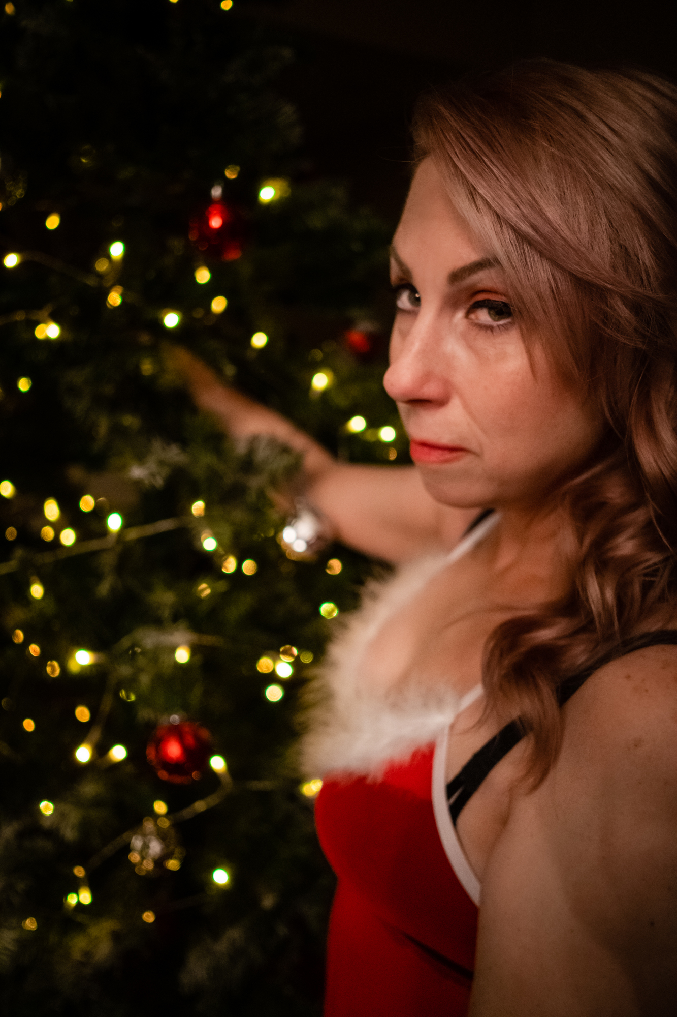 Best Christmas boudoir: Beautiful woman in festive red lingerie, reaching into a Christmas tree in a captivating holiday scene.
