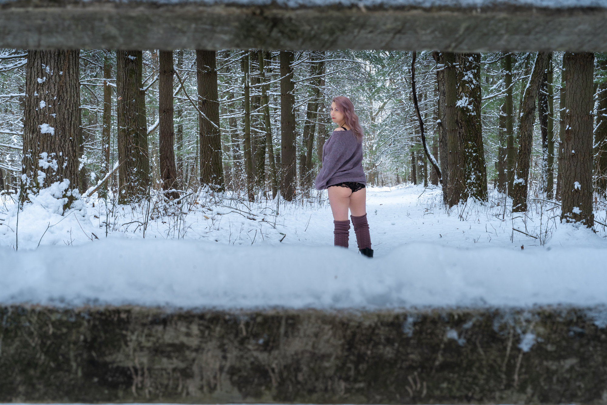 Best boudoir in nature: Woman in cozy sweater and lingerie, framed by a country fence in a snow-covered forest.