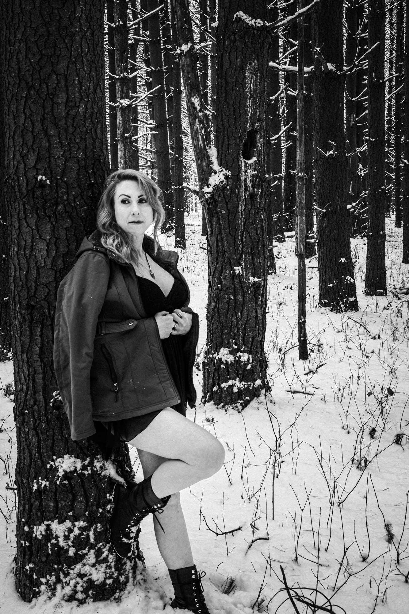 Best winter boudoir allure: Gorgeous woman in lingerie leaning against a snow-covered tree in a black and white photo.